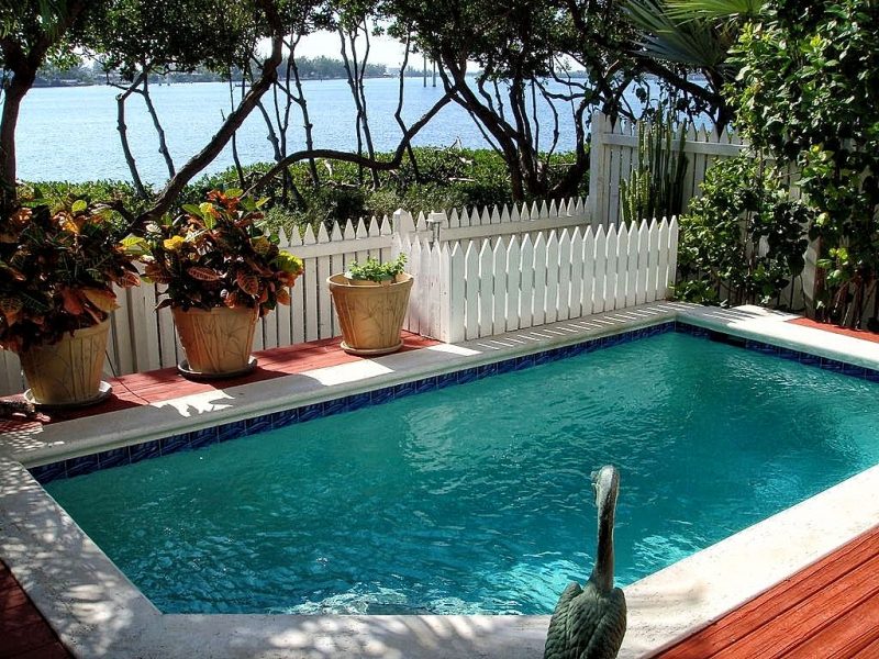 blue ceramic tile pool surround with bullnose coping and antique swan statue with patina and handcrafted planters with bamboo designs and white picket pool fence