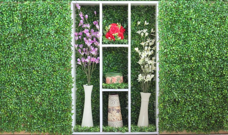 built-in painted wooden shelf with white ceramic vases and vine covered fence and decorative flowers with multi-colored vintage vases