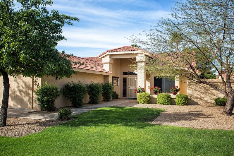 geometric gravel and grass area patterns with concrete driveway and alley to front door and hedges lining path and portico with red geraniums in glazed pots