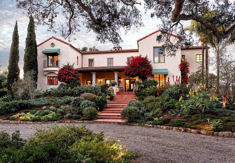 gravel driveway with stone edging and inclined parterres and terracotta-colored steps with decorative tile accents on steps and ground cover plants on lower part of parterre