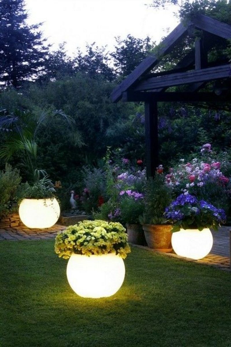 illuminated LED planters along cobblestone path and edging with dark wooden pergola and aged terra cotta planters and raised beds