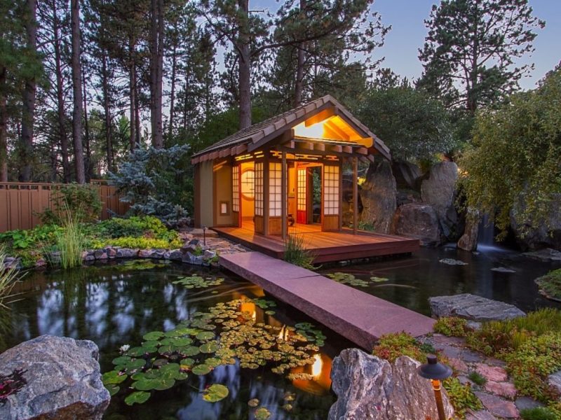 Japanese-inspired covered patio with pond and waterfall with stone slab bridge and stone and boulder pond surround