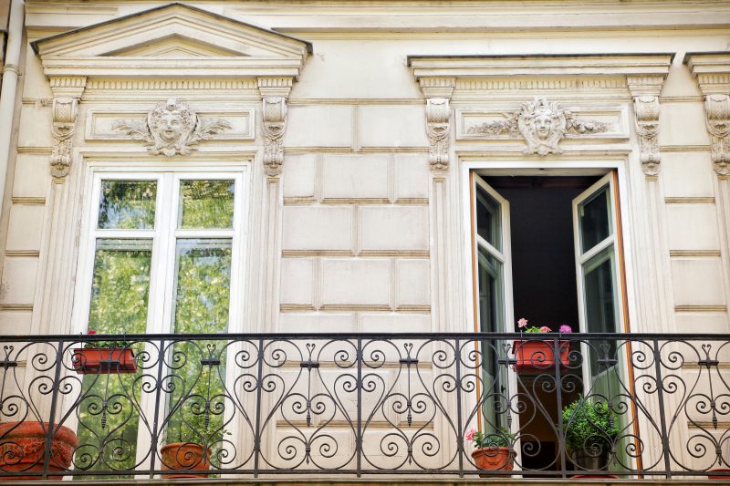 large banded Roman clay pot with matching plastic window boxes and pedimented doorways with French doors and carved stone wall and siding