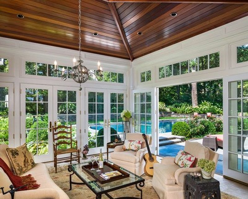multiple swing-in french doors with white muntins on transom windows and stained wood panel ceiling and globe candelabra chandelier with iron base glass top coffee table