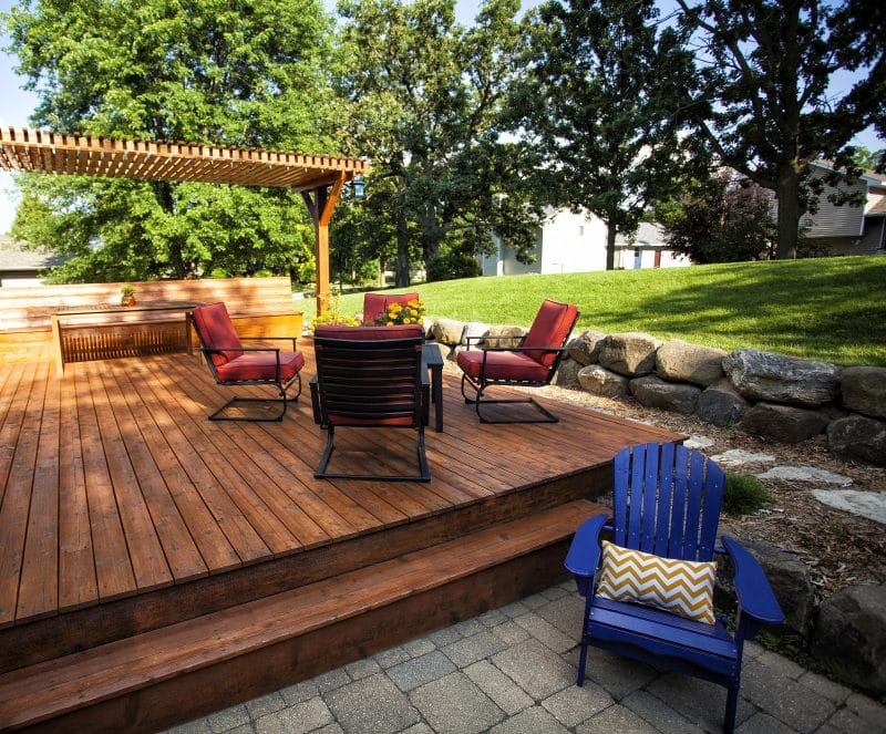 narrow pergola above built-in seating bench with 2-step wood deck and blue adirondack chair and stepping stones with stacked natural stone border