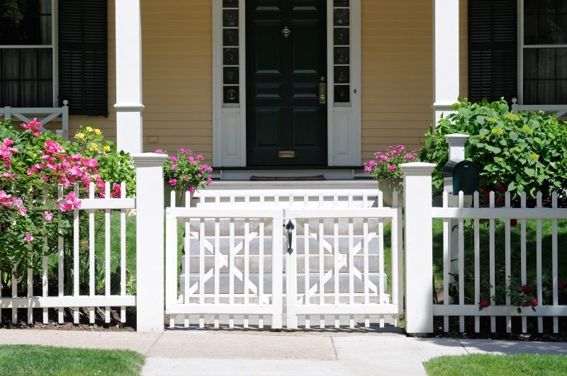 narrow pickets with modified points and low swing gate with black front door with white frame and sidelites and green mailbox and porch shutters