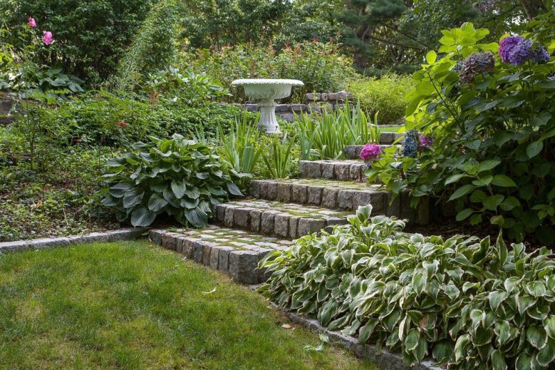 pedestal birdbath with fluted base with raised garden bed on upper level and concrete stone slabs doubling as benches and stone steps calling back the garden bed edging