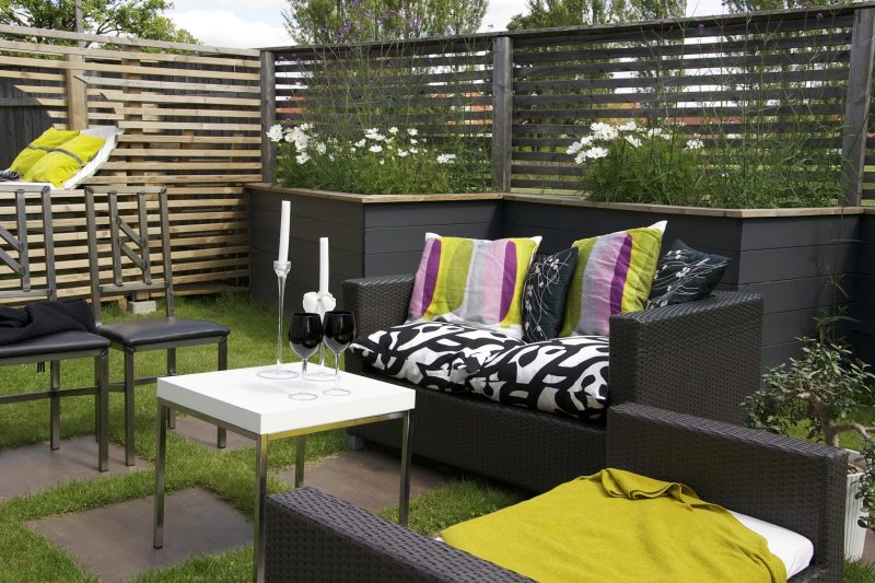privacy wall with grass between patio tiles and elevated planters with color matching outdoor furniture
