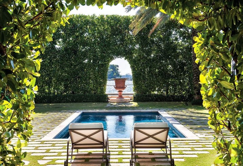 rectangular pool with blue tile edging and concrete paver with grass inserts and security hedges with boxwood and keyhole hedge opening with large antique urn