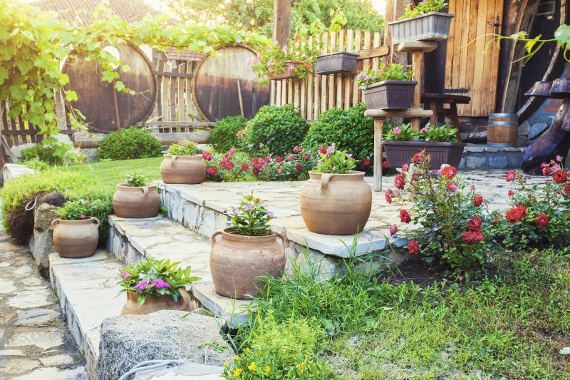 resin flower boxes with wooden plant riser and matching terracotta jar planters and natural wood convex-designed fence with large barrel covers used for additional privacy