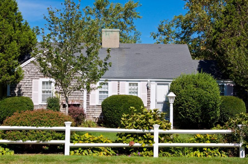 split rail white vinyl fence and aged shingle siding with white lamppost and light pink window box and single-hung windows with light pink shutters