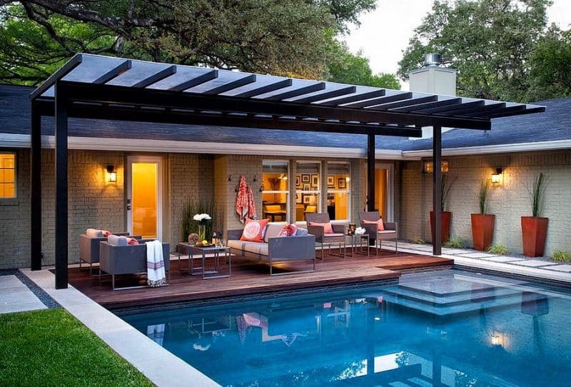 steel pergola with polycarbonate sheet roof and wooden pool deck and porcelain step stones and pool coping with gravel edging and tall tapered planters matching deck stain
