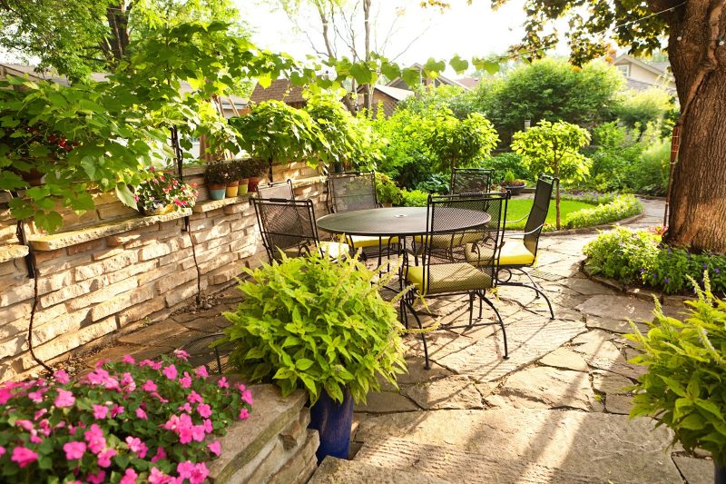 stone veneer fence with planter ledge with multi-color painted mini pots and raised bed with impatiens and blue ceramic pot with tiki torch