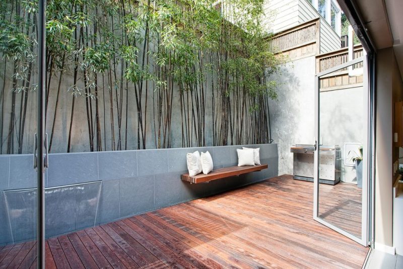 wooden deck flooring with floating built-in bench and narrow planter covering one side of patio fence and young Madake bamboo with privacy wood panel add-on
