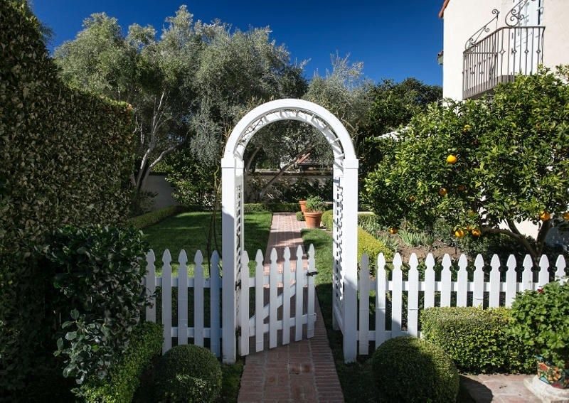wooden fence and arbor with well-manicured hedges and topiaries and lemon tree and juliette balcony with wrought iron railing and terra cotta planters