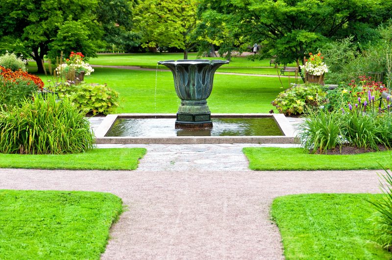 aged copper urn cascading fountain with stone base and rectangular pond stone coping with garden benches and twin urn planters on stone ledges