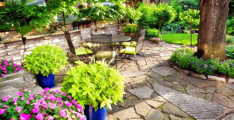 blue lapis planters with painted terracotta planters on stone floating shelf and broken flagstone patio and walkway with tree stone edging and apple green seat cushion with fairy lights on tree trunk