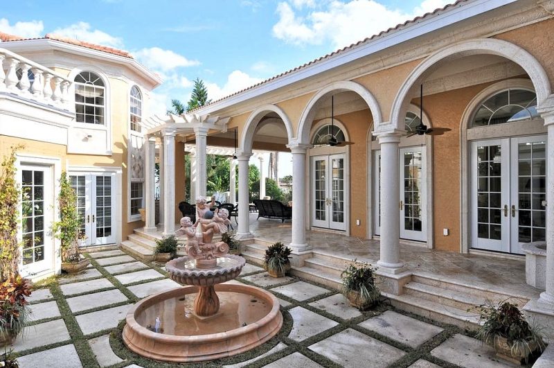 granite playful cherub fountain with scalloped top basin and concrete pavers with moss inserts and pergola designed entryway with stucco columns and arches
