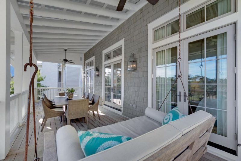 natural wood floor blending nicely with shingle siding and swing daybed bench with neutral hued cushions and turquoise throw pillows with two oil rubbed fans