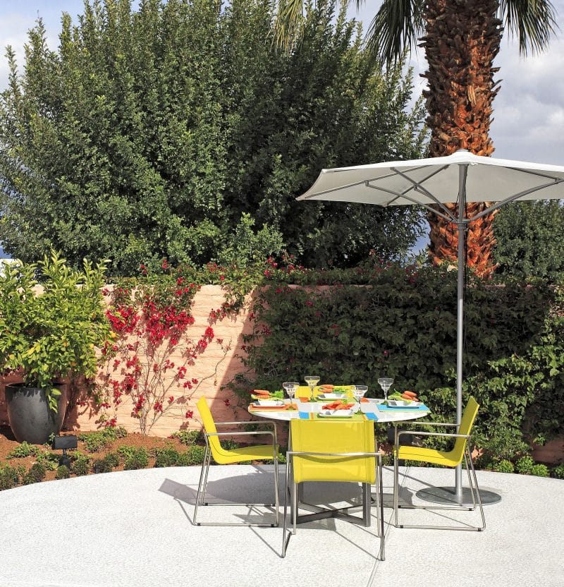 potted lemon tree on large black planter with lime steel chairs and white patio umbrella with chrome-finished stand and black garden spotlight and palm tree