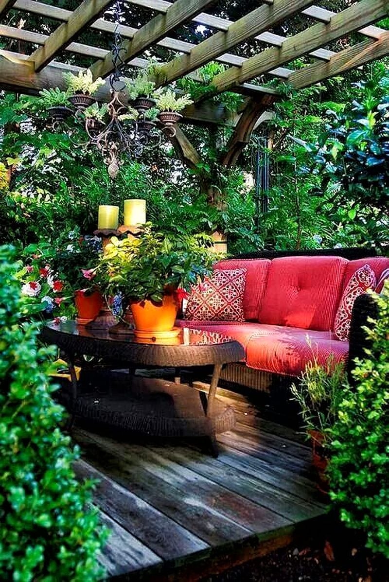 repurposed antique lantern used as mini planters with open roof pergola with deck planks and wind chimes and red with thin white pinstripes sofa cushions with glass-topped oval coffee table in textured dark chocolate weave