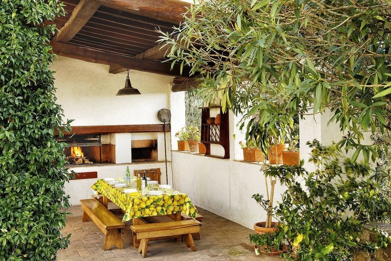 set of rectangular and classic terracotta planters on patio ledge with breakweave patio tiles and vinyl tablecloth with lemon print and exposed beam ceiling and built-in fireplace with pizza grill