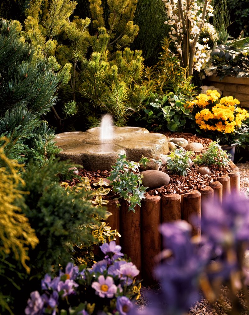 stone flower-designed disappearing fountain with crushed stone drain rocks and bamboo slats raised bed edging with pea pebble flooring
