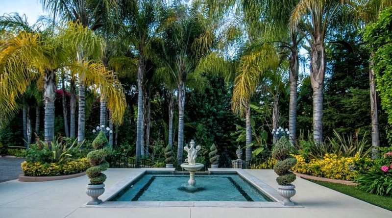 twin cherub stone cascading fountain and rectangular pool with darker tile pool inlay and stone urn planters and trimmed cypress trees with wrought iron railings