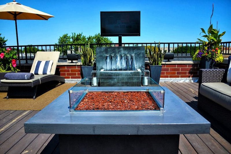 weathered zinc wall fountain 6-spout trough with tabletop fire pit and borderless glass fire pit screen with wooden deck and twin floor candle lamps