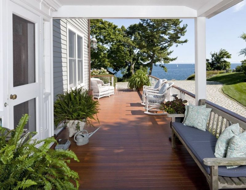 wooden board flooring calling back top of railing with weathered wooden bench and railing panels with glass inserts and side entry to the porch with antique galvanized zinc watering can