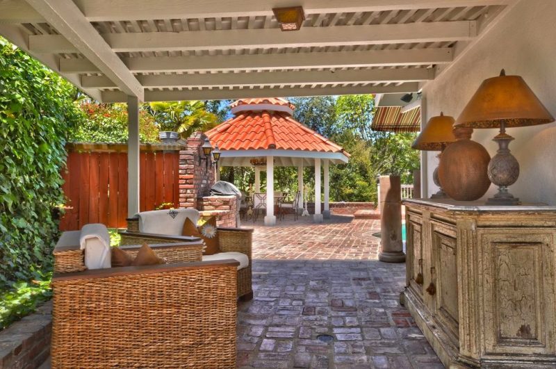 brick basketweave flooring with 2 wicker armchairs with white cushions and wood armrests with large antique weathered sideboard with white marble countertop and antique bronze lampshade base