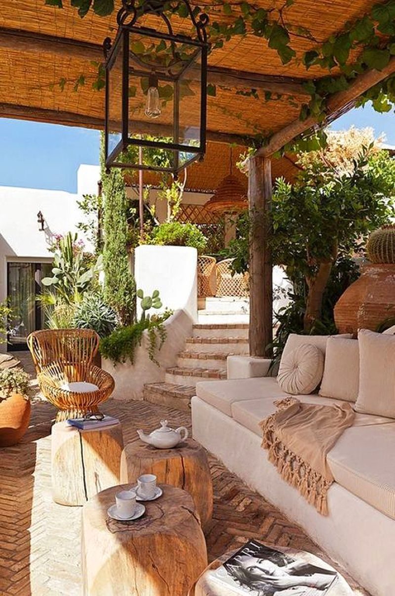 herringbone brick floor with brick stair steps and 4 log stools doubling as coffee tables and built-in white concrete sofa with beige cushions and round bamboo chair with white cushion and glass lantern pendant light