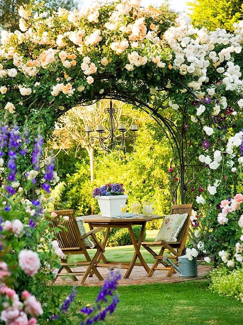 hexagonal tea table set with throw pillows and Victorian-inspired chandelier with climbing peach white roses and clematis “etoile violette” (i.e. purple star in French) with wrought iron arbor and galvanized zinc watering can