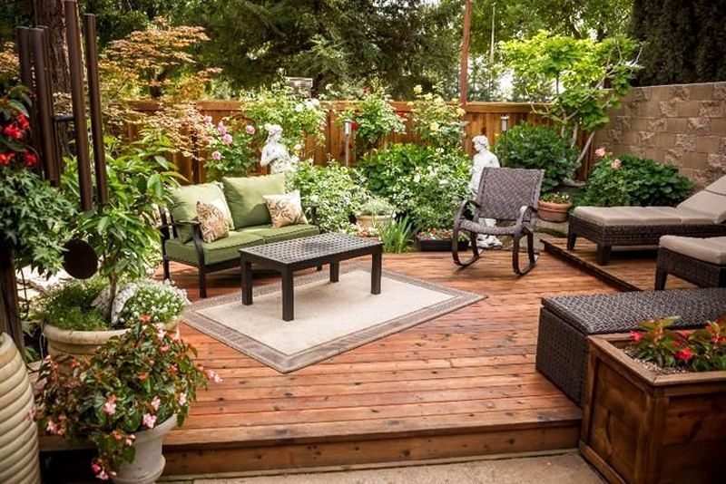 medium-toned wood panel fence and alternating smooth and rough gray stone brick wall with 2 rattan sun loungers and wicker storage bench calling back the rocking chair and raised wood box planter with redwood deck flooring