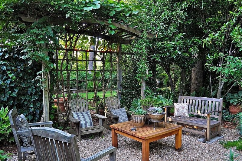 pea gravel patio area with low-apron wooden chairs with rustic cushion and succulents and Crassula on clay pots and English ivy entwined with Moonflower on aged wood arbor with a matching lattice privacy wall and warm tone fairy lights