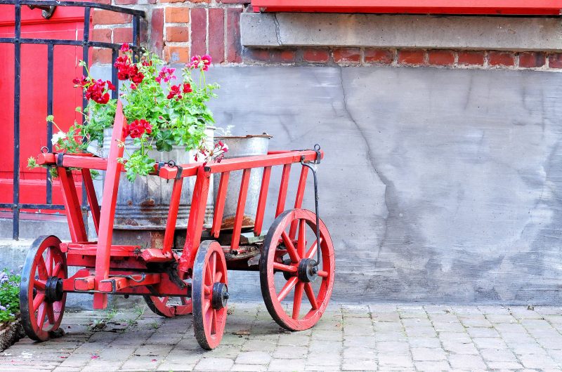 red wagon planter with matching red wooden front door and repurposed zinc buckets with red geranium matching wagon