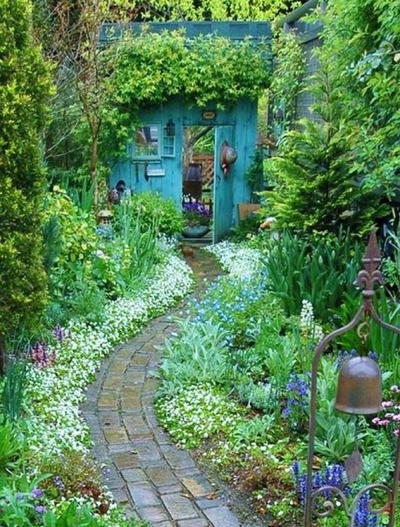 turquoise wooden facade and door with antique ornamental iron bell and little window with shutters and flower-lined cobblestone path with small pagoda and duck statues with tall wooden fence