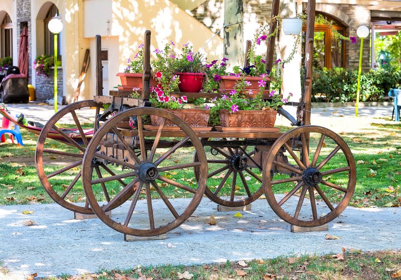wagon planter with wooden wheel stopper and rose Picotee and Peppy Cerise petunias with leaf-carved terracotta flower boxes and white resin pot hanging from wagon’s rear end beams
