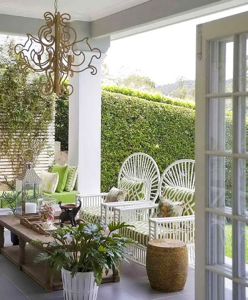 white slatted wood fence panel and privacy hedge fen with 2 white round back bamboo chairs with moss green and white patterned cushions and built-in bench with green cushion and two-tiered bare wooden coffee table