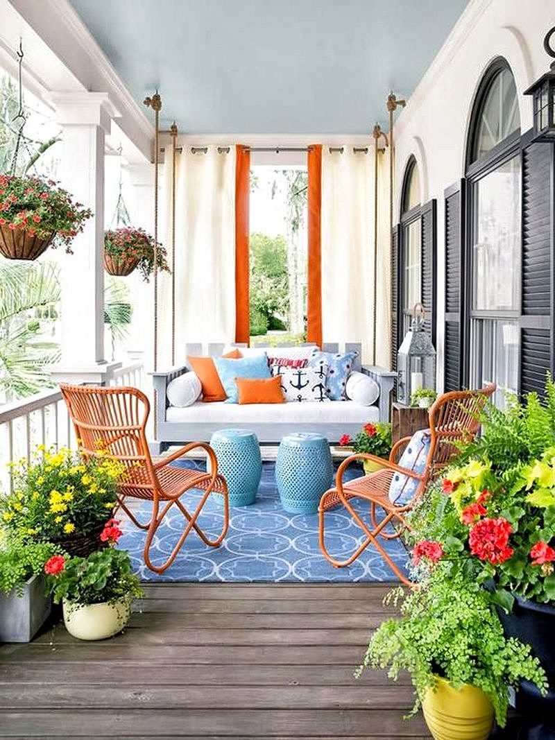 2 hanging baskets with million bells and light gray hanging porch swing bed with orange hand woven Rizza chair and 2 powder blue ceramic lattice garden stools doubling as coffee tables and black window shutters