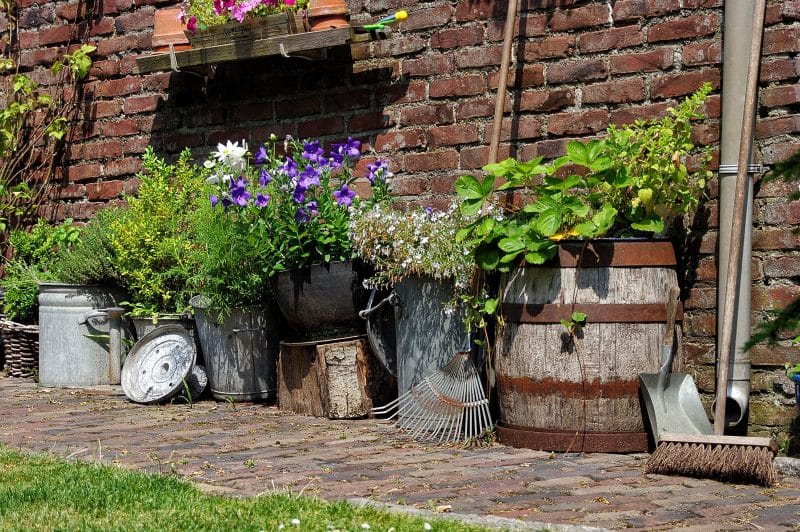 aged hogshead barrel planter with recycled wooden tray and zinc water containers used as planters with DIY wooden shelf with repurposed rattan basket and brick garden path