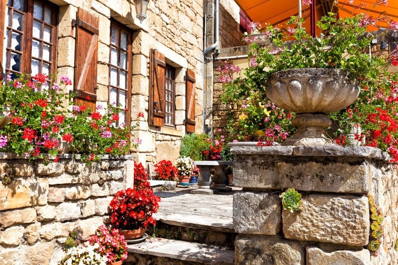 antique stone urn planter with begonias pots and stacked stone fence with growing rosette Succulents and Z-style wooden shutters with outdoor front door lantern