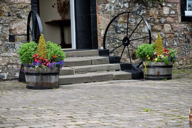 double half barrels with painted wagon wheels with 9 spokes doubling up as stair railing and cement pavers with stone siding and concrete steps with edges painted in black