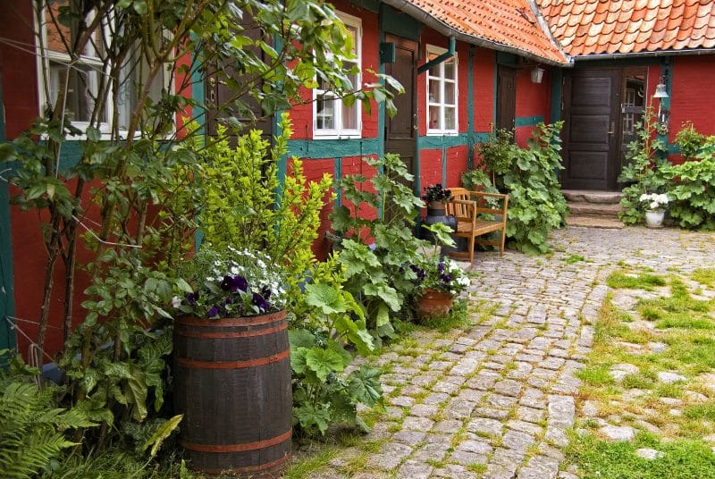 full-sized dark wood barrel and swing out windows with painted wooden siding with green accents and cobblestone pavers with wooden garden bench