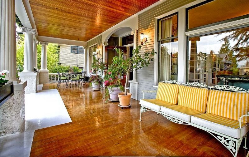 fuschias in white planters with rolling planter caddies and white reeded pillars with rough concrete base and white wrought iron sofa with two-tone high gloss finished hardwood floor