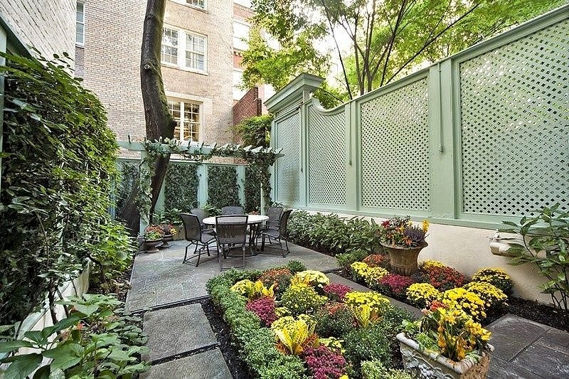 hand carved clay pot in center of garden bed with vertical garden and mint green wooden lattice fence panels with mint green pergola and stamped concrete flooring with matching stepping stone garden path