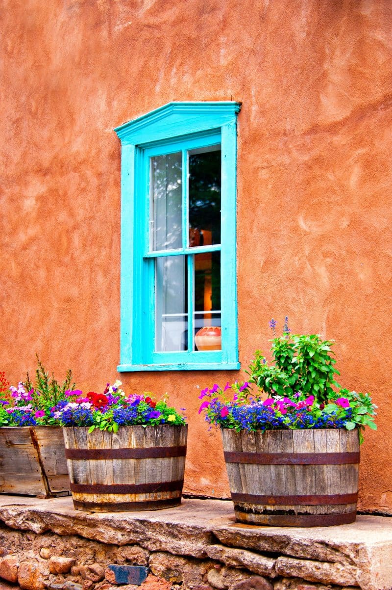 pair of rustic half drum planters and wooden DIY trough planter with blue salvia and dash stucco siding in a terracotta shade with aqua window sill and sashes