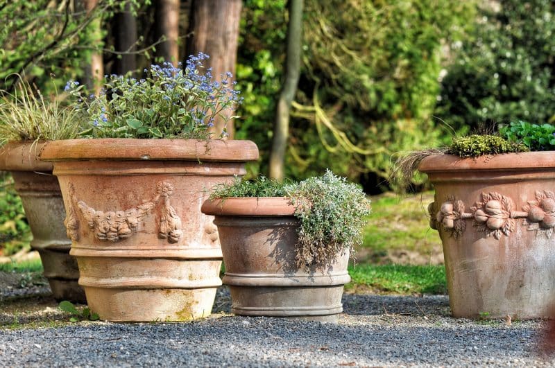 rolled rim cylinder planters with bands and handcrafted fruit designs and blue lobelia with pea gravel patio flooring