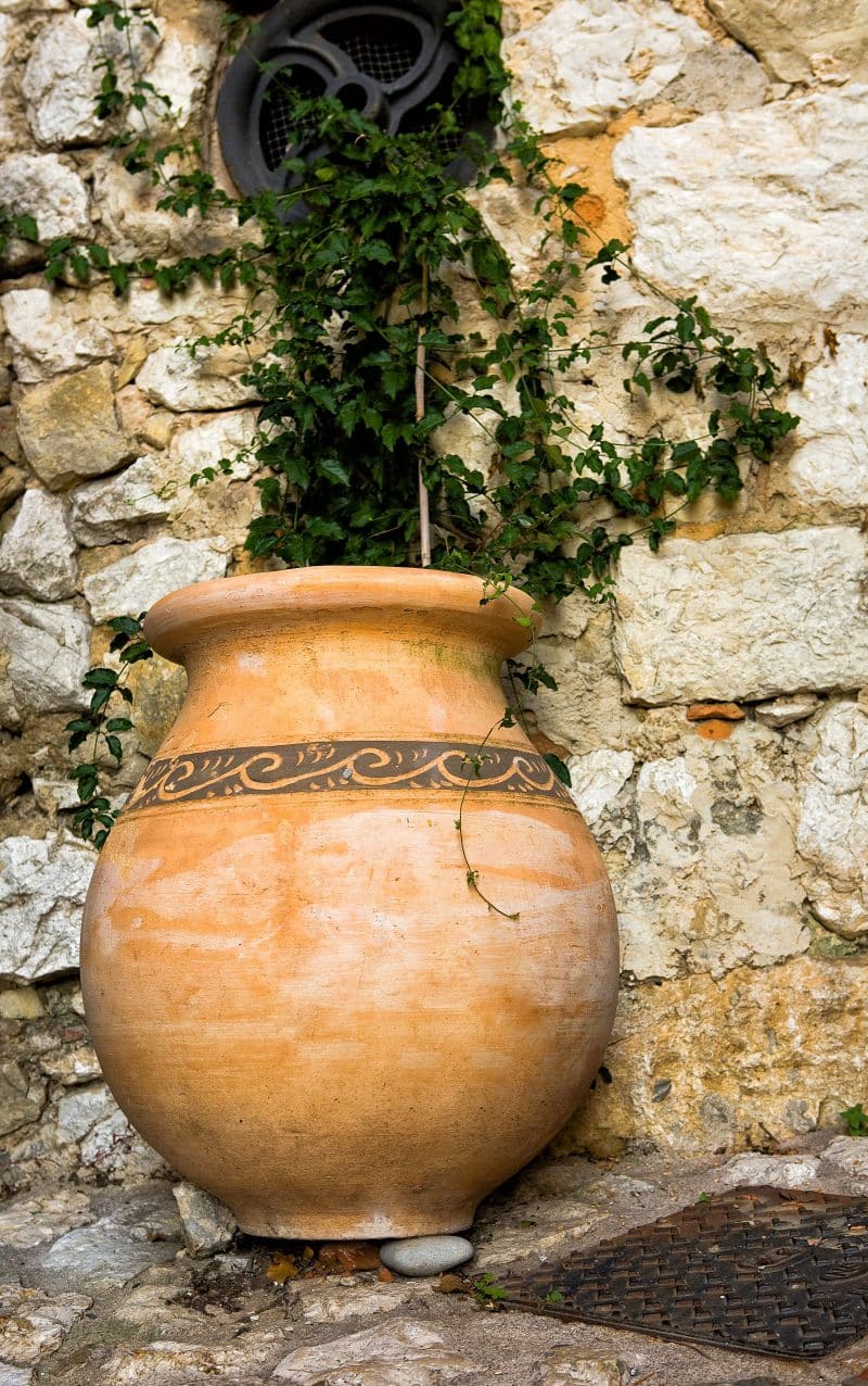 rolled rim terracotta water jar repurposed as planter and stenciled design on jar and mortared stone wall with circular screen window with metal insert