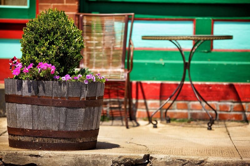 vintage half oak barrel with brick siding with red green and sky blue wood siding accents and aluminum garden chair and table in a bronze finish
